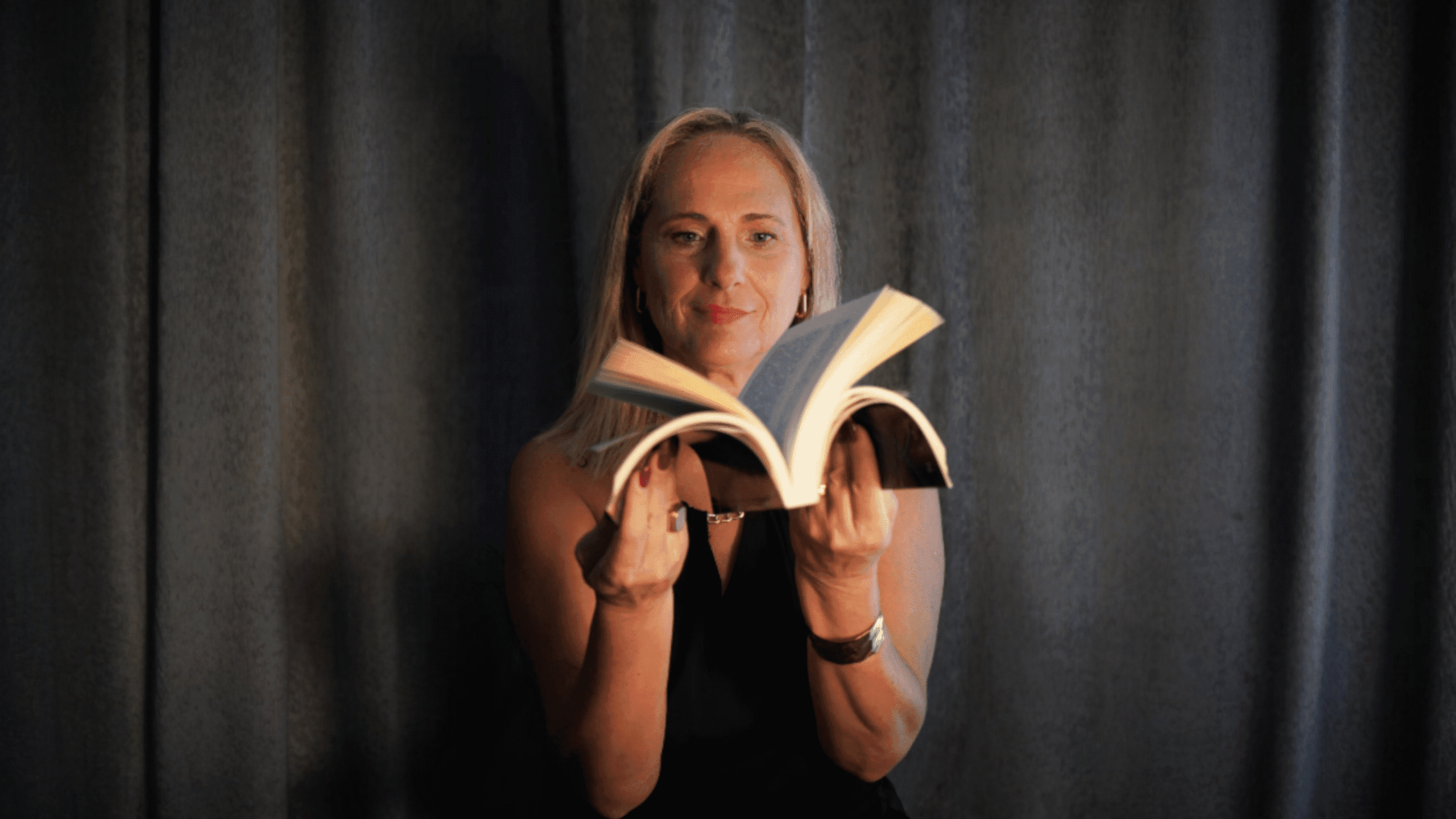 Carla Ornelas a segurar um livro aberto, contra um fundo escuro.
